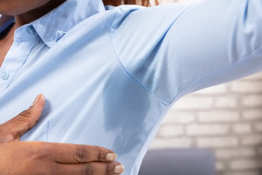Ein großer Schweißfleck unter dem Arm zeichnet sich auf dem Hemd ab