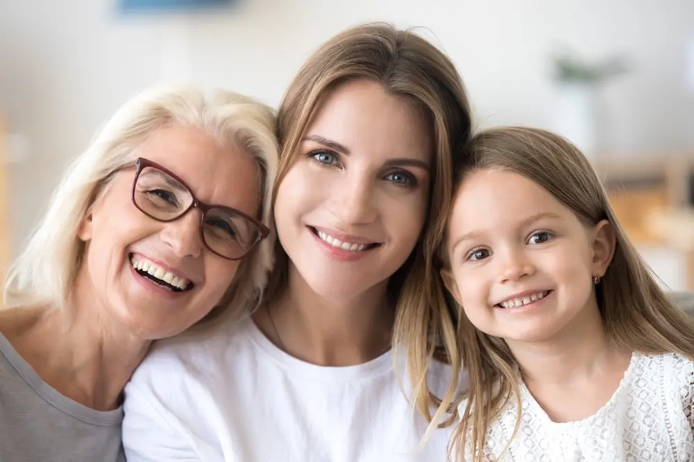 Familie mit Oma, Mutter und Kind schauen glücklich in die Kamera